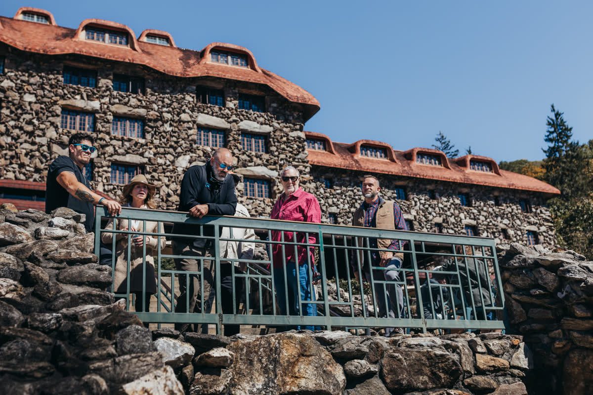 A tour group gathered at the rail below a historic stone lodge